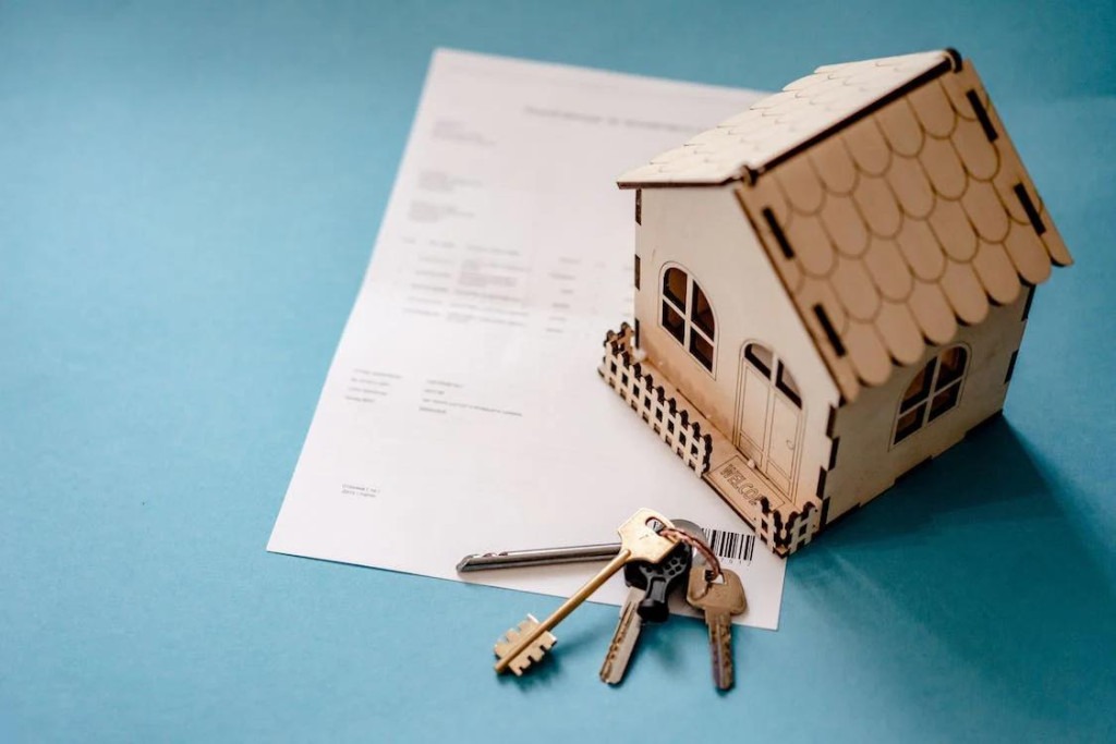 An image of a miniature wooden house, keys, and contract on a table 
