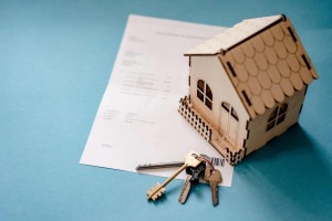 An image of a miniature wooden house, keys, and contract on a table