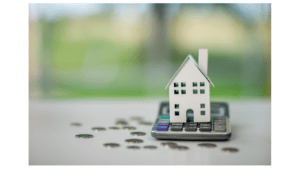 Model house on calculator with scattered coins, representing rental income and DSCR loan qualification in Colorado