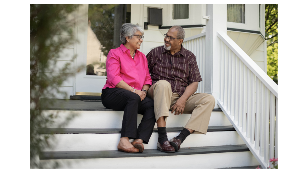 Elderly couple smiling on front porch steps after moving into a new home purchased using a Family Opportunity Mortgage in Colorado.