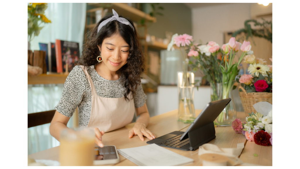 Young woman running a small business (florist/crafts) reviewing her finances and bank statements on her phone and tablet.